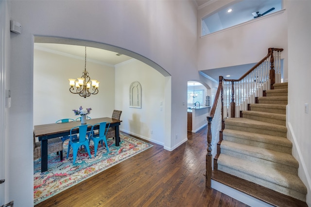 foyer with ornamental molding, a chandelier, wood finished floors, arched walkways, and stairway