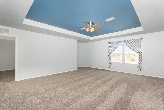 unfurnished room with a raised ceiling, a ceiling fan, carpet floors, and crown molding
