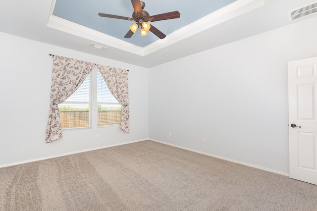 carpeted spare room featuring a tray ceiling, ceiling fan, and baseboards