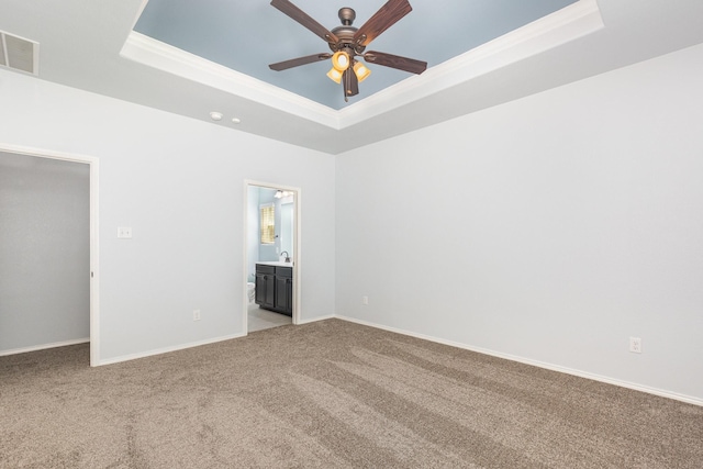 unfurnished bedroom with a tray ceiling, light carpet, baseboards, and ensuite bathroom