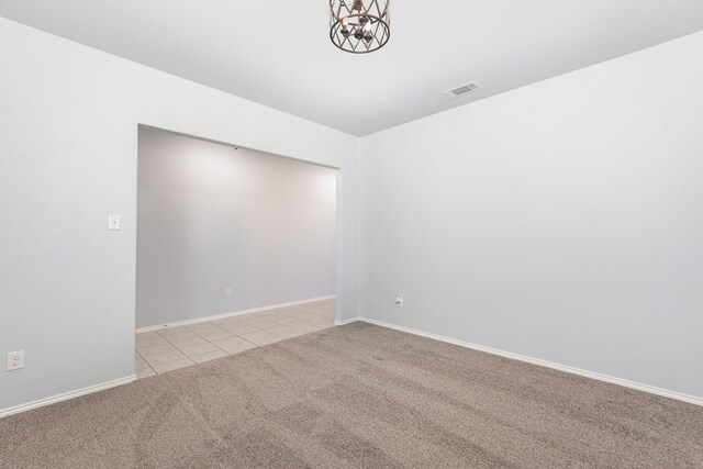 empty room featuring light carpet, light tile patterned floors, a chandelier, and baseboards