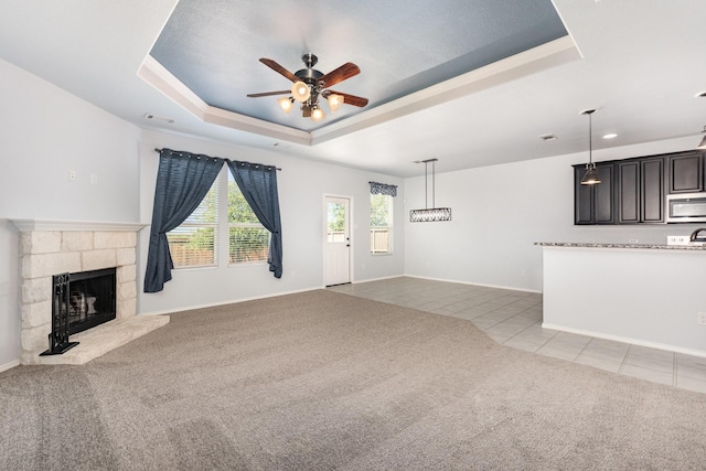 unfurnished living room featuring carpet, a raised ceiling, a ceiling fan, and tile patterned floors