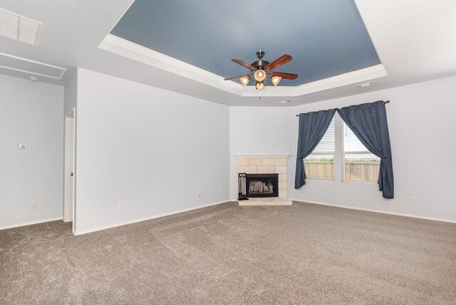 unfurnished living room with a tray ceiling, carpet, ceiling fan, a stone fireplace, and baseboards