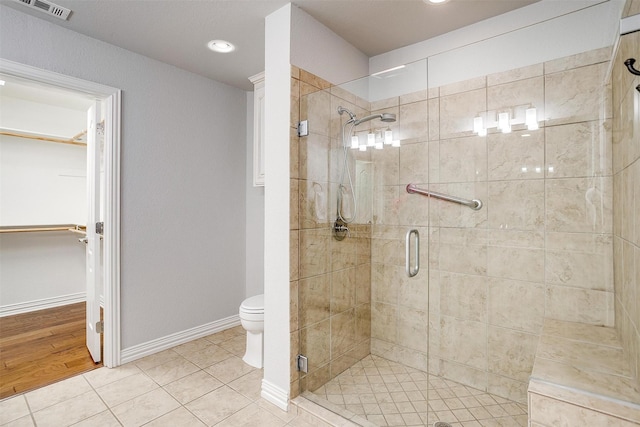 bathroom with a stall shower, toilet, tile patterned floors, baseboards, and a walk in closet