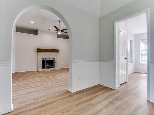 unfurnished living room featuring a ceiling fan, arched walkways, light wood finished floors, a fireplace, and recessed lighting
