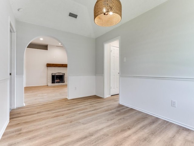 spare room featuring arched walkways, vaulted ceiling, light wood finished floors, a brick fireplace, and baseboards
