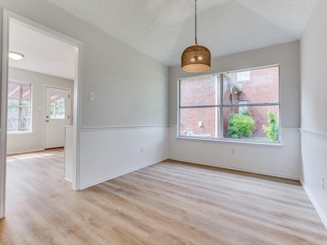 unfurnished dining area with healthy amount of natural light, light wood finished floors, a textured ceiling, and baseboards