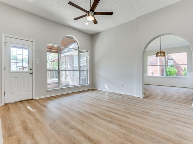 foyer entrance featuring arched walkways, a ceiling fan, light wood-style flooring, a textured ceiling, and baseboards
