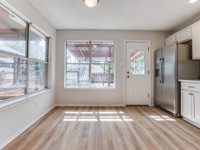 unfurnished dining area with light wood-style floors, baseboards, and a textured ceiling