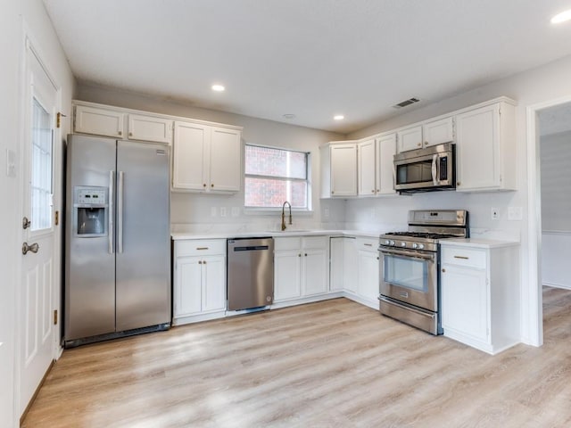 kitchen featuring appliances with stainless steel finishes, a sink, light countertops, white cabinetry, and light wood-style floors