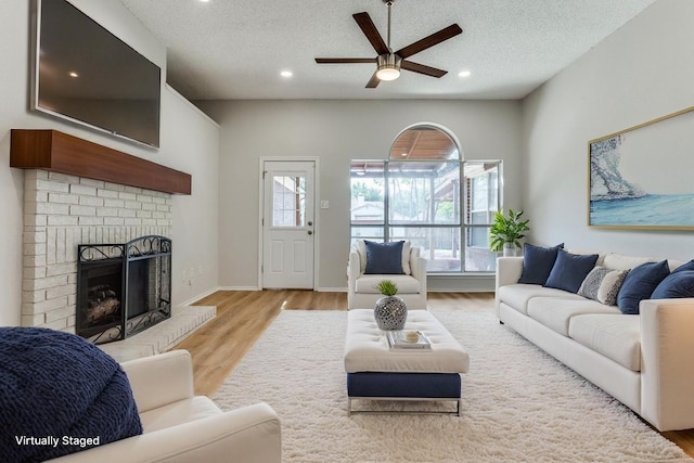 living room with a ceiling fan, a brick fireplace, a textured ceiling, wood finished floors, and recessed lighting