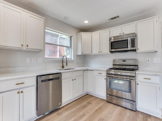 kitchen with appliances with stainless steel finishes, a sink, white cabinets, light wood finished floors, and recessed lighting