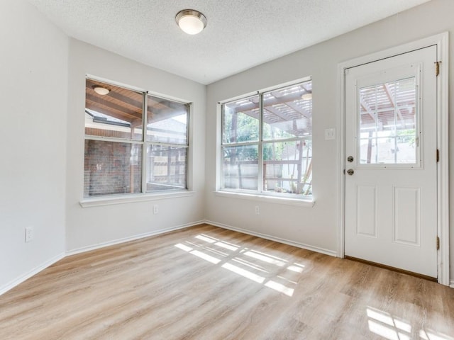 unfurnished dining area featuring light wood-type flooring, a textured ceiling, and baseboards