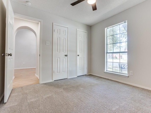 unfurnished bedroom with carpet flooring, two closets, a textured ceiling, baseboards, and ceiling fan