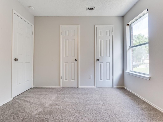 unfurnished bedroom with carpet, multiple closets, baseboards, and a textured ceiling