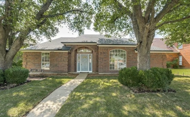 view of front facade featuring a front yard, brick siding, and a shingled roof