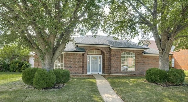 view of front facade featuring a front lawn, brick siding, and roof with shingles