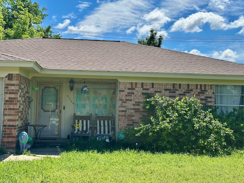 doorway to property featuring brick siding, a porch, and roof with shingles