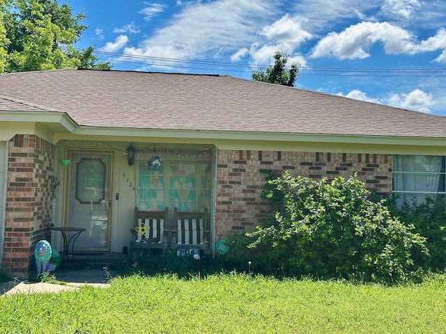doorway to property featuring brick siding, a porch, and roof with shingles