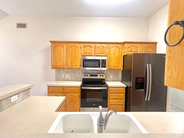 kitchen with stainless steel appliances, a sink, tasteful backsplash, and light countertops