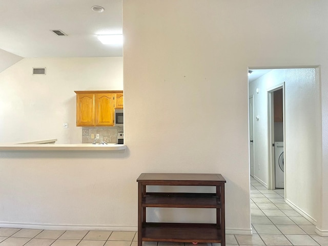 interior space featuring washer / clothes dryer, light countertops, light tile patterned floors, tasteful backsplash, and stainless steel microwave