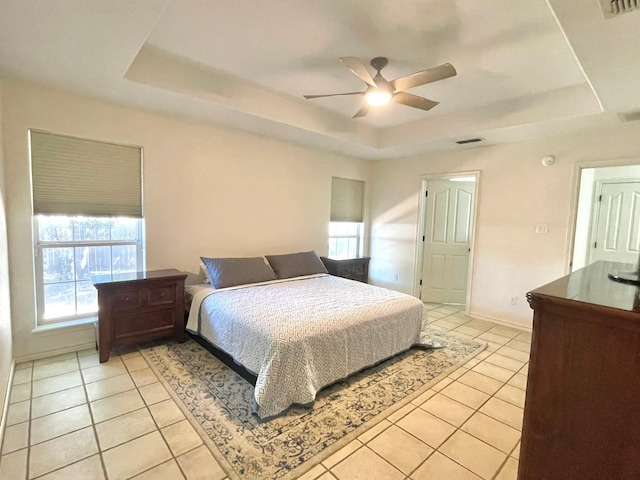 bedroom featuring a tray ceiling, light tile patterned flooring, a ceiling fan, and baseboards