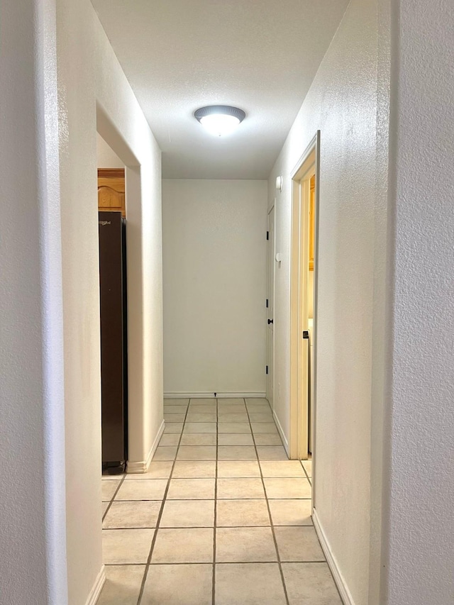 hallway with light tile patterned floors, baseboards, and a textured wall