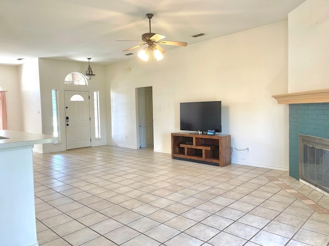 unfurnished living room with light tile patterned floors, ceiling fan, a brick fireplace, and baseboards