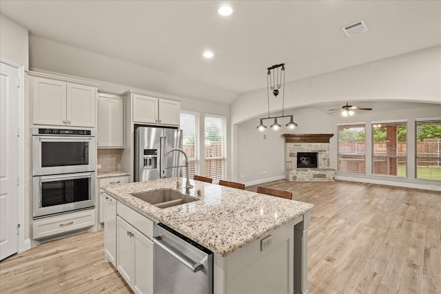 8325 Western, The Colony, TX 75056 - kitchen featuring appliances with stainless steel finishes, a sink, a fireplace, a ceiling fan, and light wood-style floors