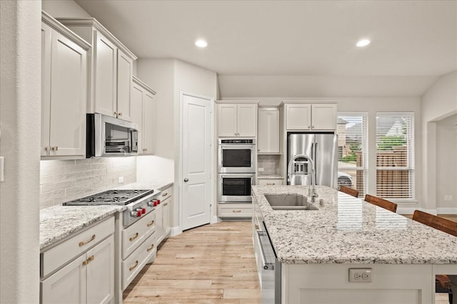 8325 Western, The Colony, TX 75056 - kitchen with appliances with stainless steel finishes, a sink, a kitchen island with sink, light wood-type flooring, and backsplash