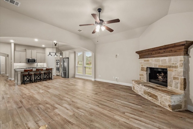 8325 Western, The Colony, TX 75056 - unfurnished living room featuring vaulted ceiling, a stone fireplace, light wood-style floors, a ceiling fan, and baseboards