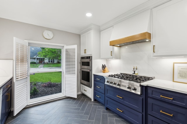 kitchen featuring appliances with stainless steel finishes, blue cabinets, white cabinetry, backsplash, and premium range hood