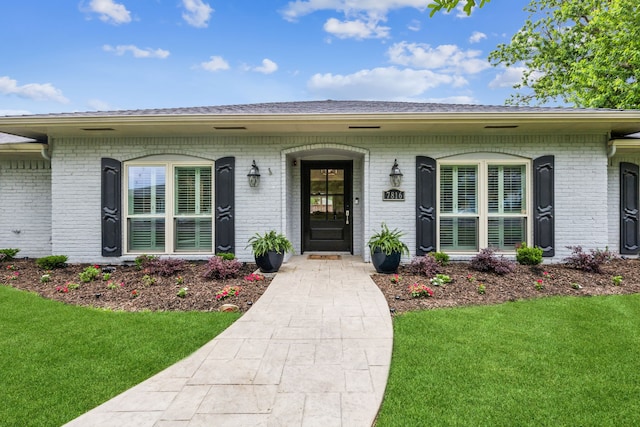 view of exterior entry featuring a lawn, brick siding, and a porch