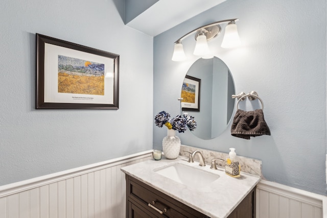 bathroom with a wainscoted wall, vanity, and a decorative wall