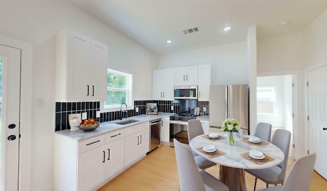402 Perry Ave, Waxahachie, TX 75165 - kitchen with appliances with stainless steel finishes, a sink, backsplash, white cabinets, and light wood-style floors