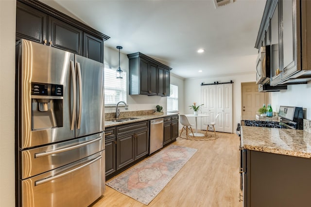 kitchen featuring appliances with stainless steel finishes, a sink, light wood finished floors, crown molding, and light stone countertops