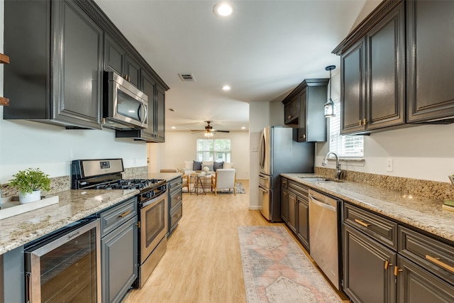 kitchen featuring appliances with stainless steel finishes, a sink, wine cooler, light wood-type flooring, and open floor plan