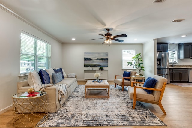 living area with crown molding, light wood-style floors, a ceiling fan, baseboards, and recessed lighting