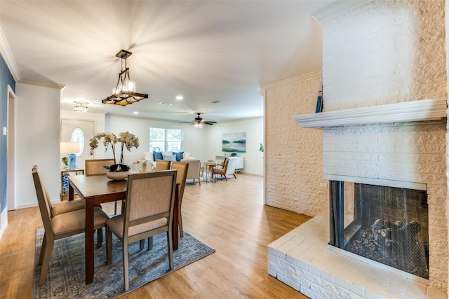 dining space with light wood-type flooring, a fireplace, a ceiling fan, and ornamental molding
