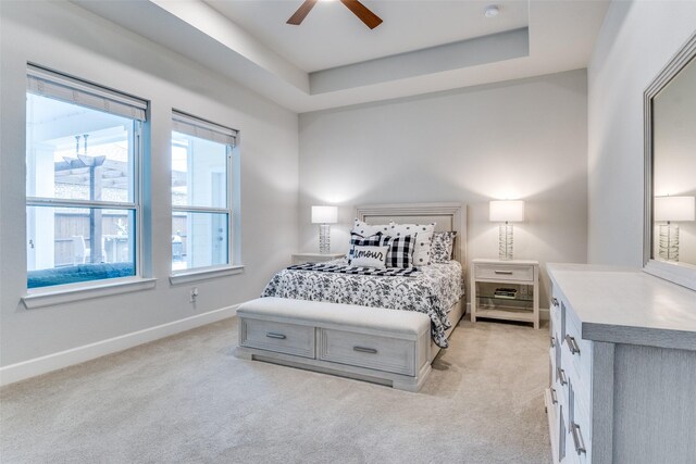 bedroom featuring light colored carpet, baseboards, a tray ceiling, and ceiling fan