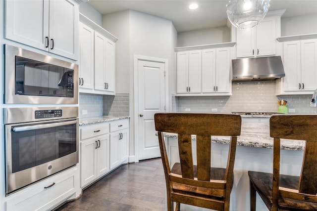 kitchen with stainless steel appliances, under cabinet range hood, decorative backsplash, light stone counters, and recessed lighting