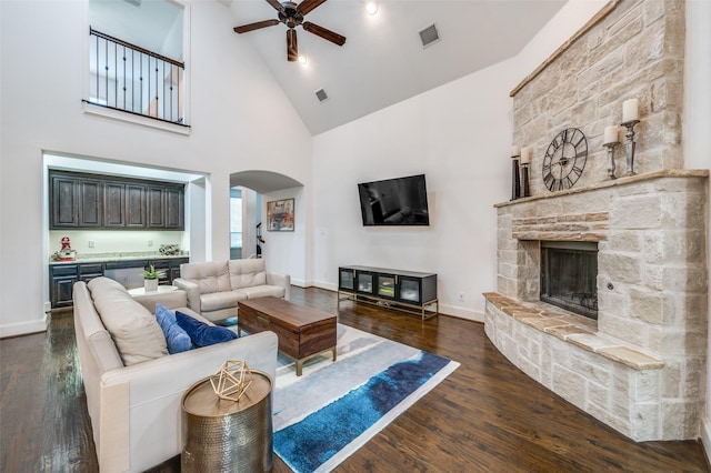 living room with arched walkways, ceiling fan, dark wood-type flooring, high vaulted ceiling, and a stone fireplace