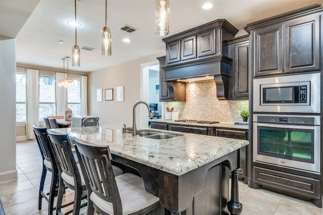 kitchen with appliances with stainless steel finishes, a sink, backsplash, light stone counters, and a chandelier