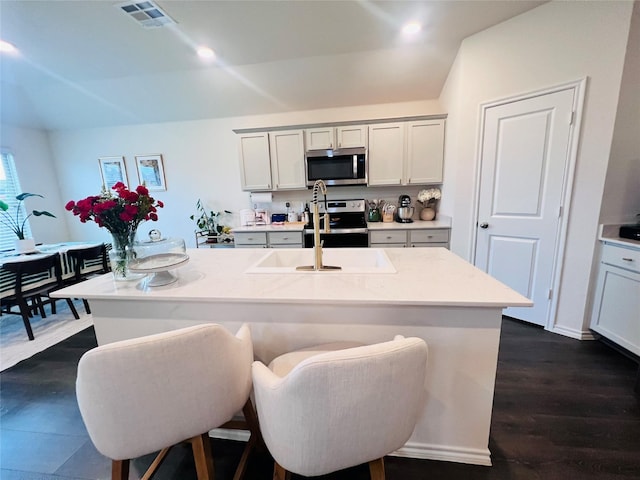 kitchen featuring stainless steel appliances, light countertops, a kitchen island with sink, a breakfast bar area, and dark wood-style floors