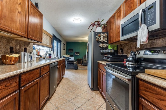2818 Ashglen Dr, Garland, TX 75043 - kitchen with stainless steel appliances, a sink, decorative backsplash, brown cabinets, and a textured ceiling