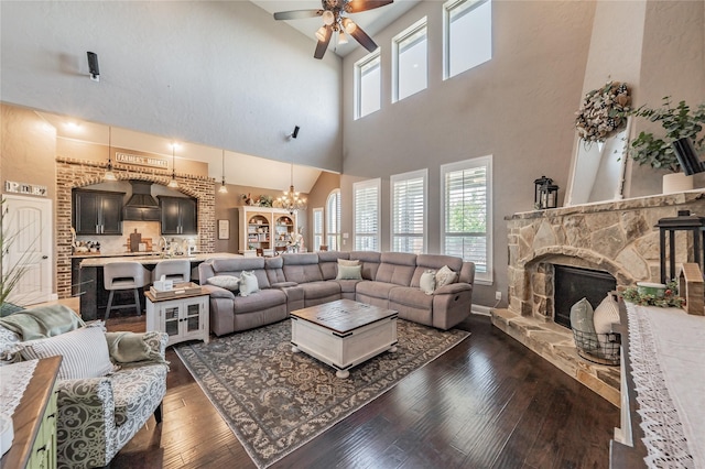 1212 Teton Dr, Burleson, TX 76028 - living room with a towering ceiling, a chandelier, a ceiling fan, dark wood-style floors, and a stone fireplace