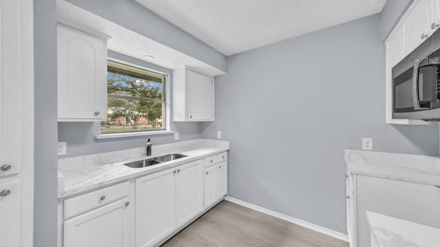 2017 Moline Dr, Haltom City, TX 76117 - kitchen featuring a sink, stainless steel microwave, light wood-style flooring, white cabinetry, and light stone counters