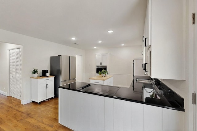 53 Devonshire Dr, Bedford, TX 76021 - kitchen featuring black electric cooktop, a peninsula, freestanding refrigerator, white cabinetry, and light wood-style floors