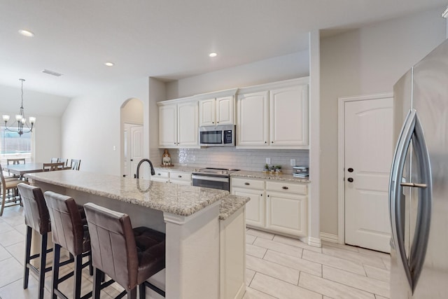 160 Melbourne Dr, Willow Park, TX 76087 - kitchen with stainless steel appliances, decorative backsplash, a kitchen bar, white cabinets, and arched walkways