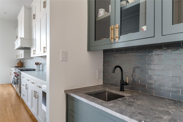 kitchen with high end stainless steel range oven, backsplash, a sink, and dark stone counters